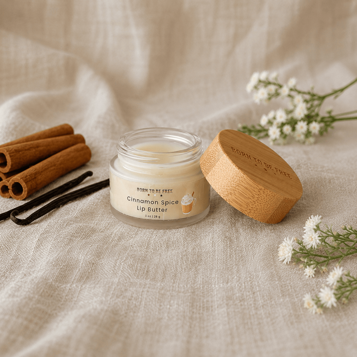 Cinnamon Spice Tallow Lip Butter in a jar with wooden lid, surrounded by cinnamon sticks and flowers.