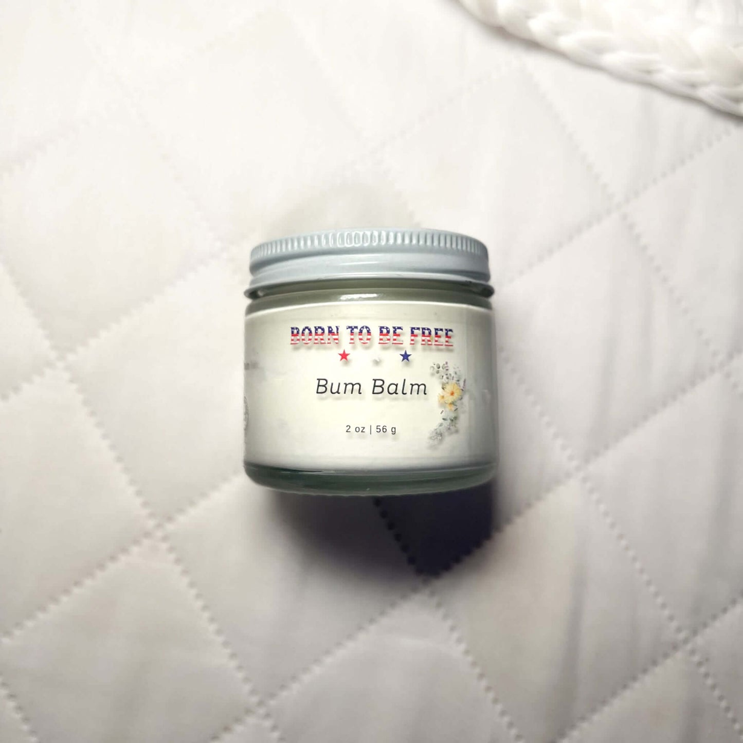 Bum Balm - Baby Diaper Cream with Tallow + Zinc in a 2 oz jar on a soft quilted background.