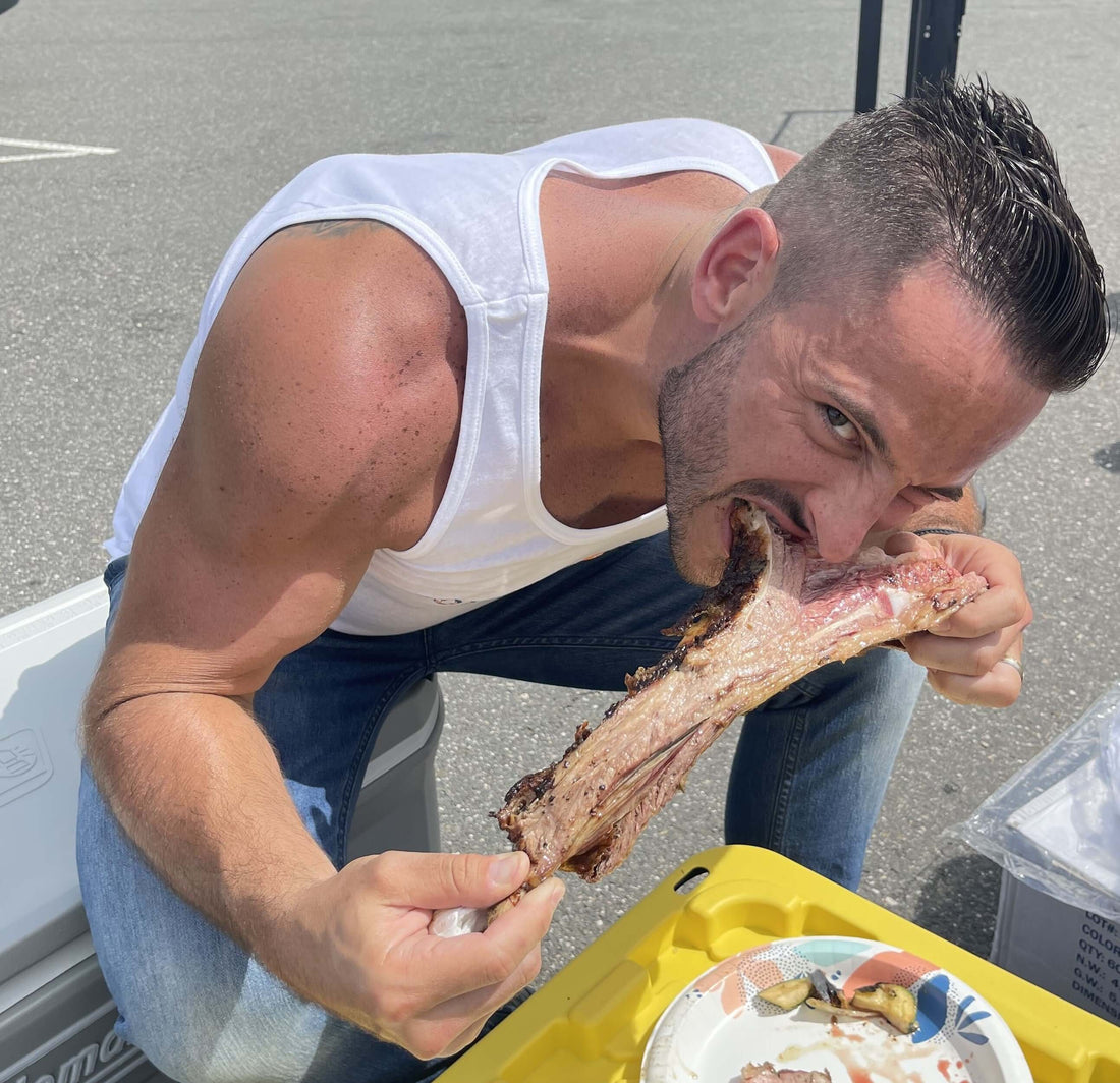 Man enjoying a large piece of meat while sitting outdoors, focused on the delicious food. Source Of The Seed