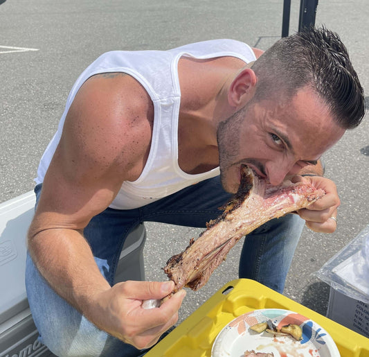 Man enjoying a large piece of meat while sitting outdoors, focused on the delicious food. Source Of The Seed