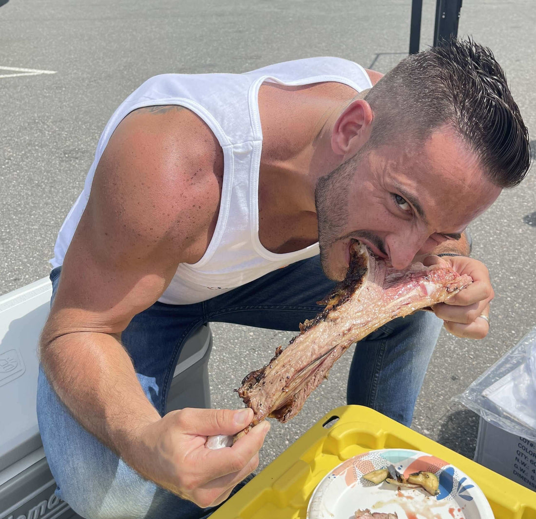 Man enjoying a large piece of meat while sitting outdoors, focused on the delicious food. Source Of The Seed