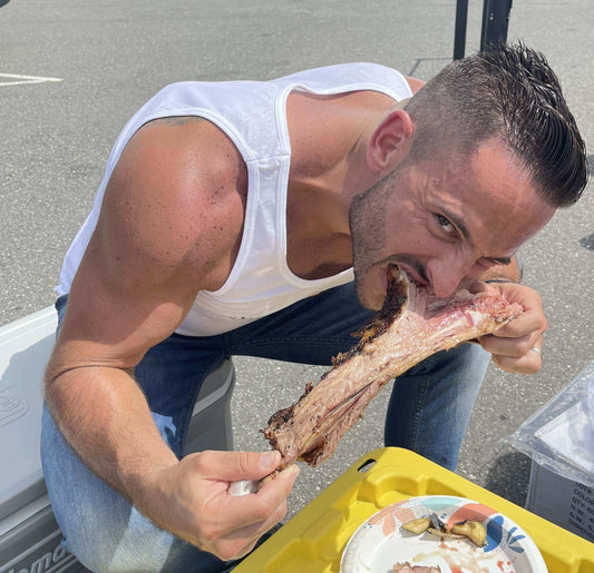 Man enjoying a large piece of meat while sitting outdoors, focused on the delicious food. Source Of The Seed