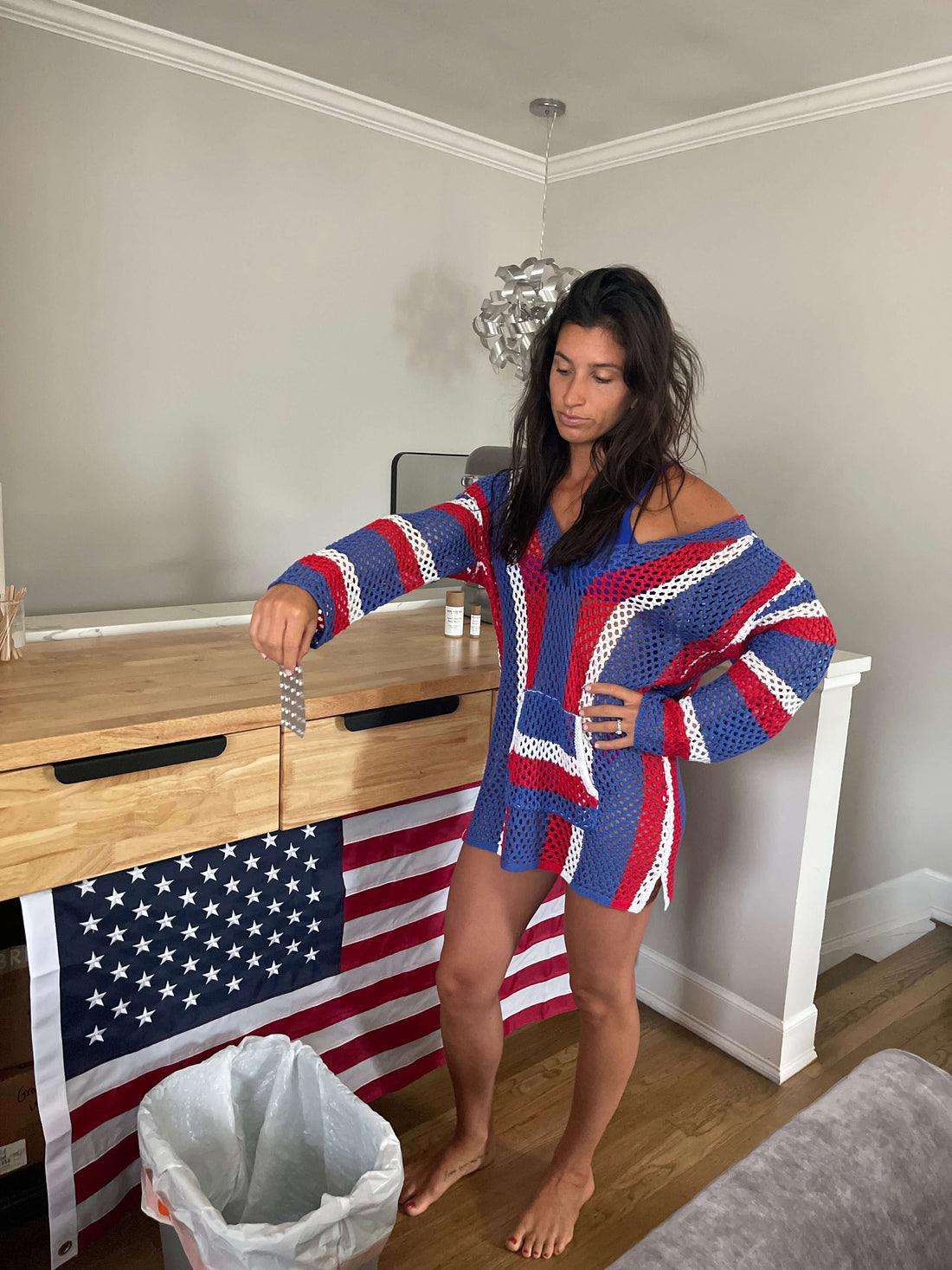 Woman in a red, white, and blue sweater standing by a trash can with an American flag in the background. The Hidden Truth About Hormonal Birth Control