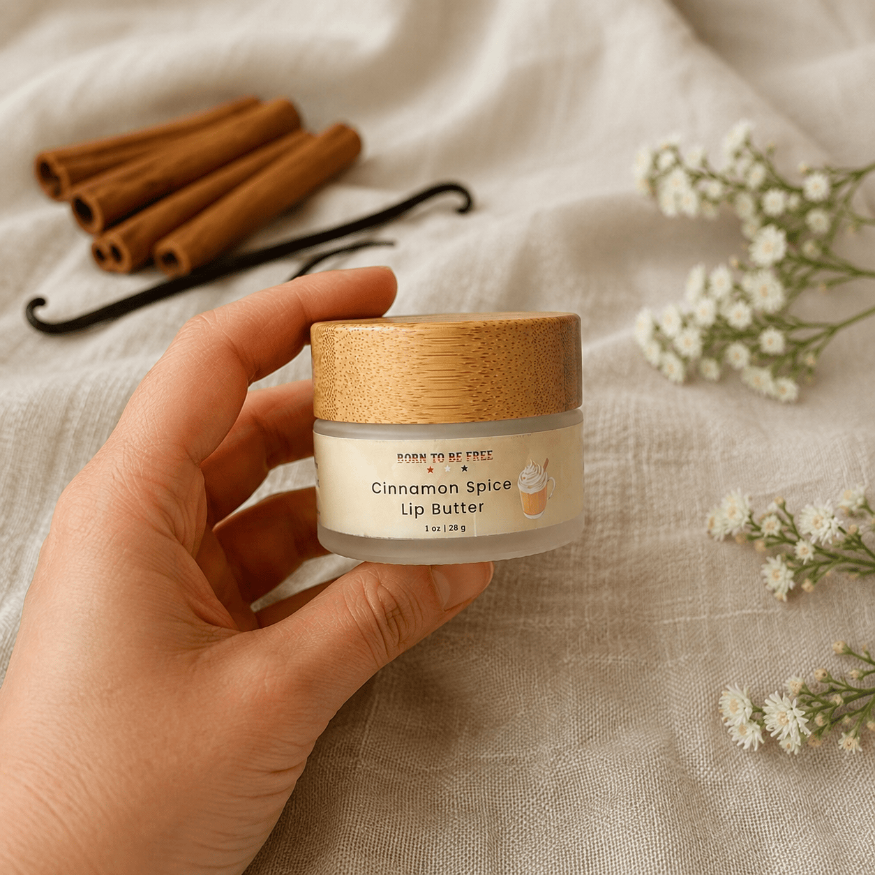 Cinnamon Spice Tallow Lip Butter jar held in hand with cinnamon sticks and flowers in the background.