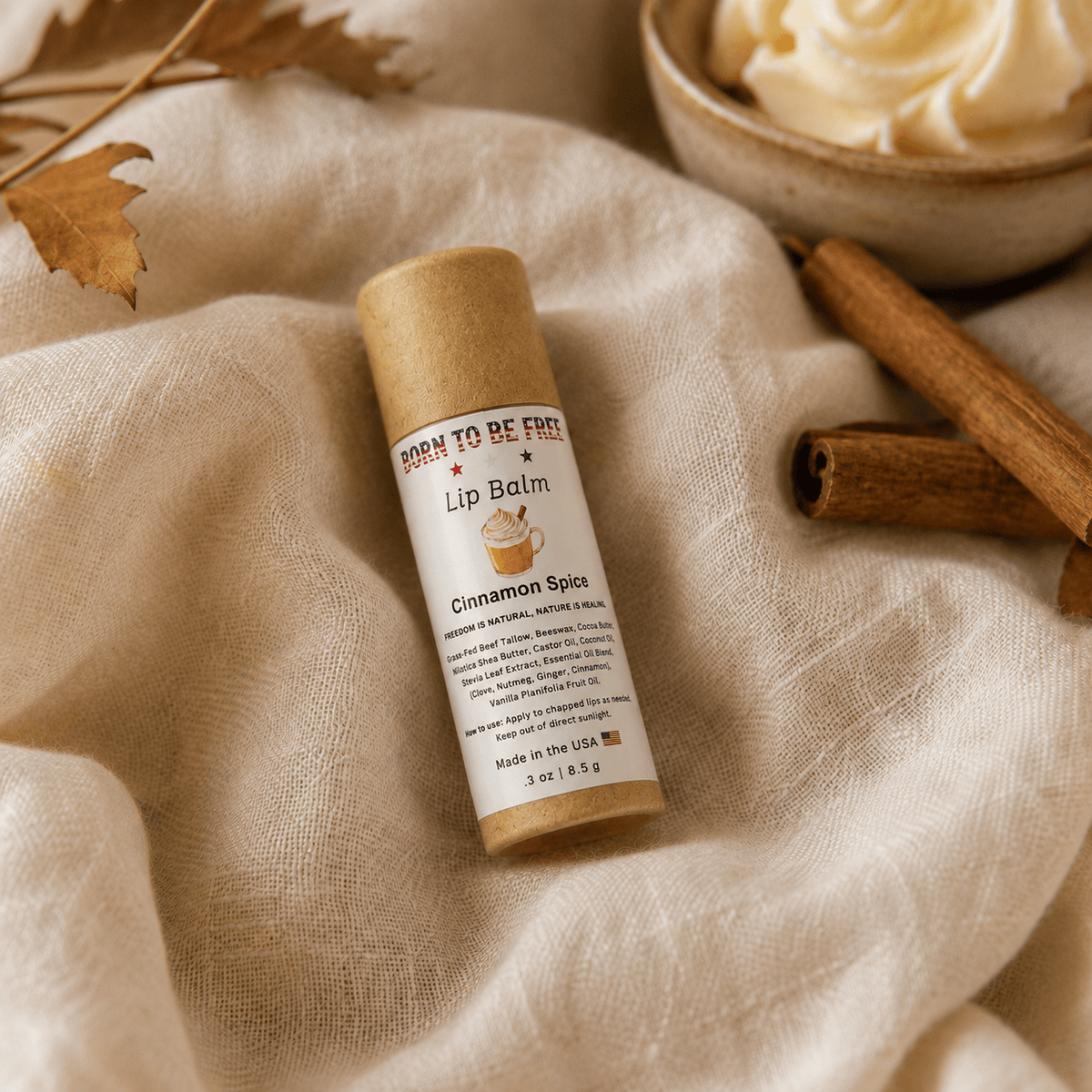 Cinnamon Spice Lip Balm tube on soft fabric with cinnamon sticks and a decorative cup.