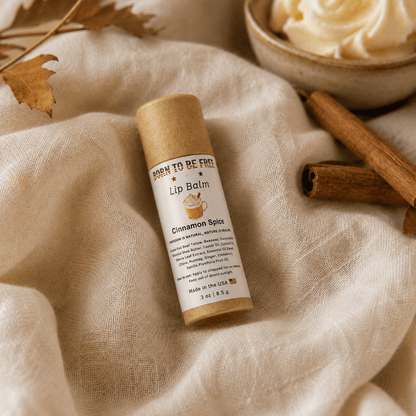 Cinnamon Spice Lip Balm tube on soft fabric with cinnamon sticks and a decorative cup.