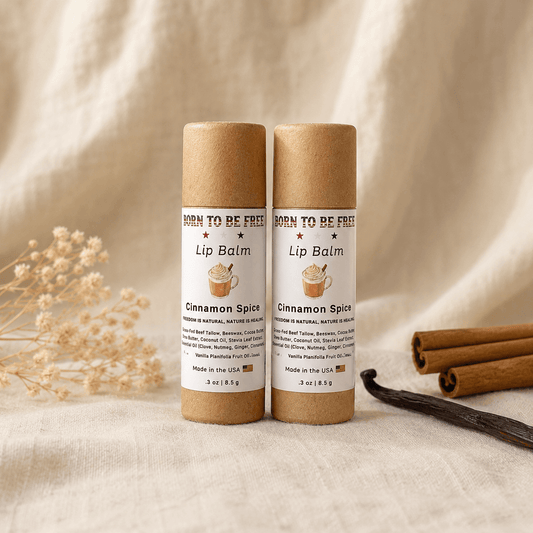 Cinnamon Spice Lip Balm tubes displayed on a soft surface with cinnamon sticks and dried flowers.
