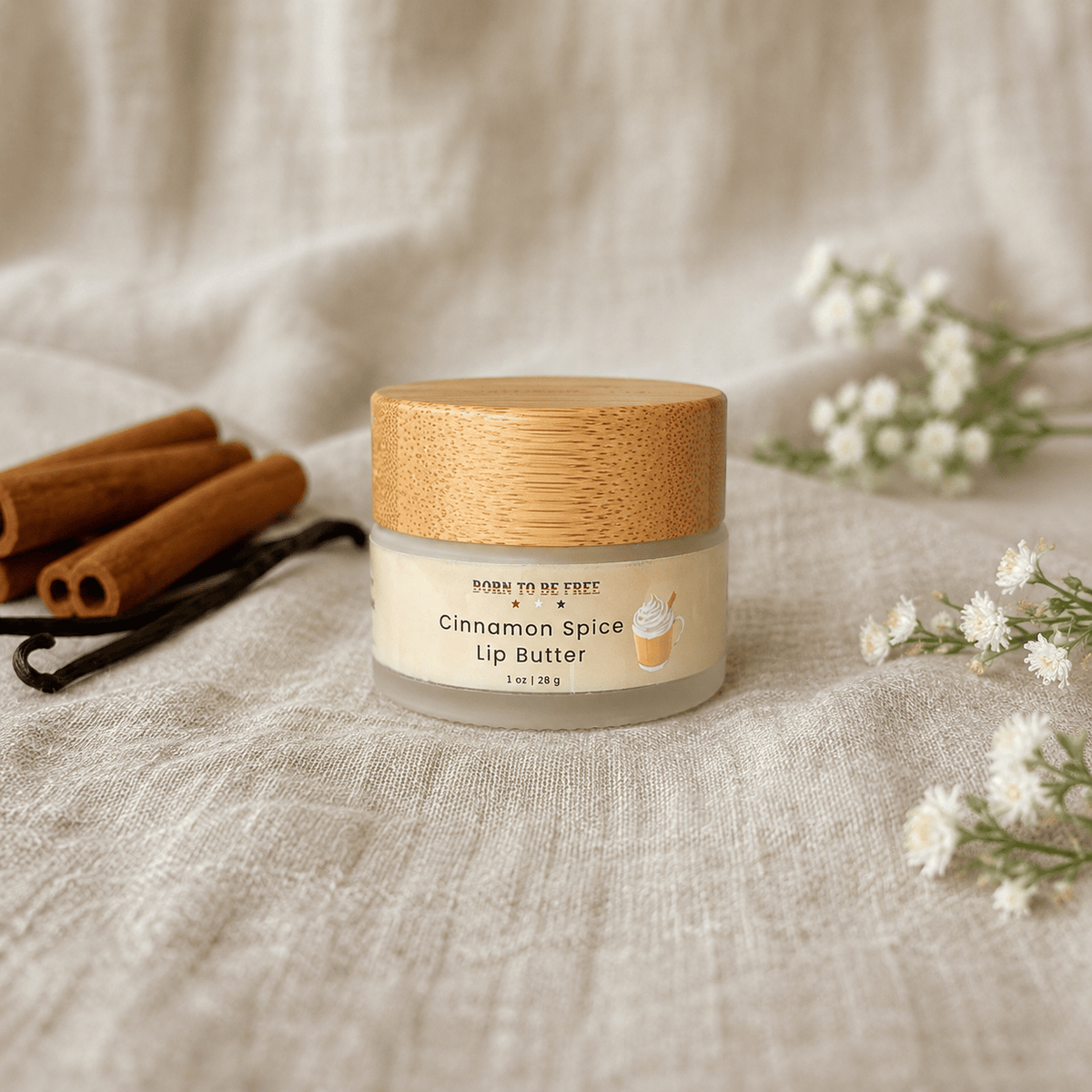 Cinnamon Spice Tallow Lip Butter in a jar with a wooden lid, surrounded by cinnamon sticks and flowers.