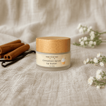 Cinnamon Spice Tallow Lip Butter in a jar with a wooden lid, surrounded by cinnamon sticks and flowers.
