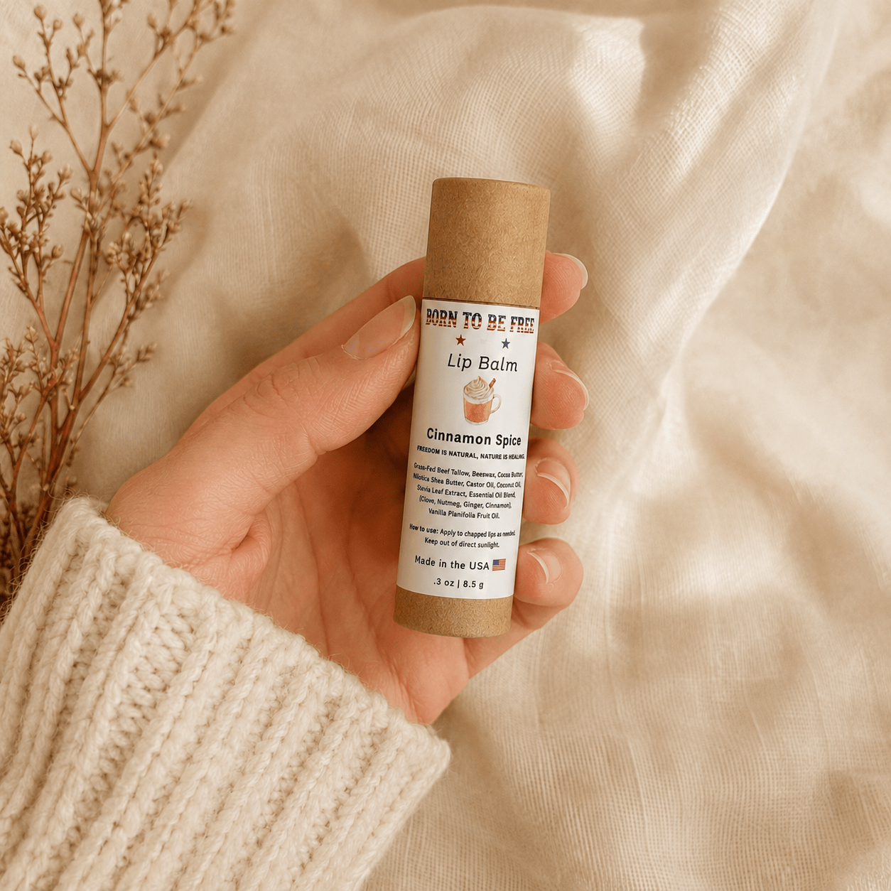 Hand holding a Cinnamon Spice Lip Balm in a eco-friendly tube on a soft fabric background.