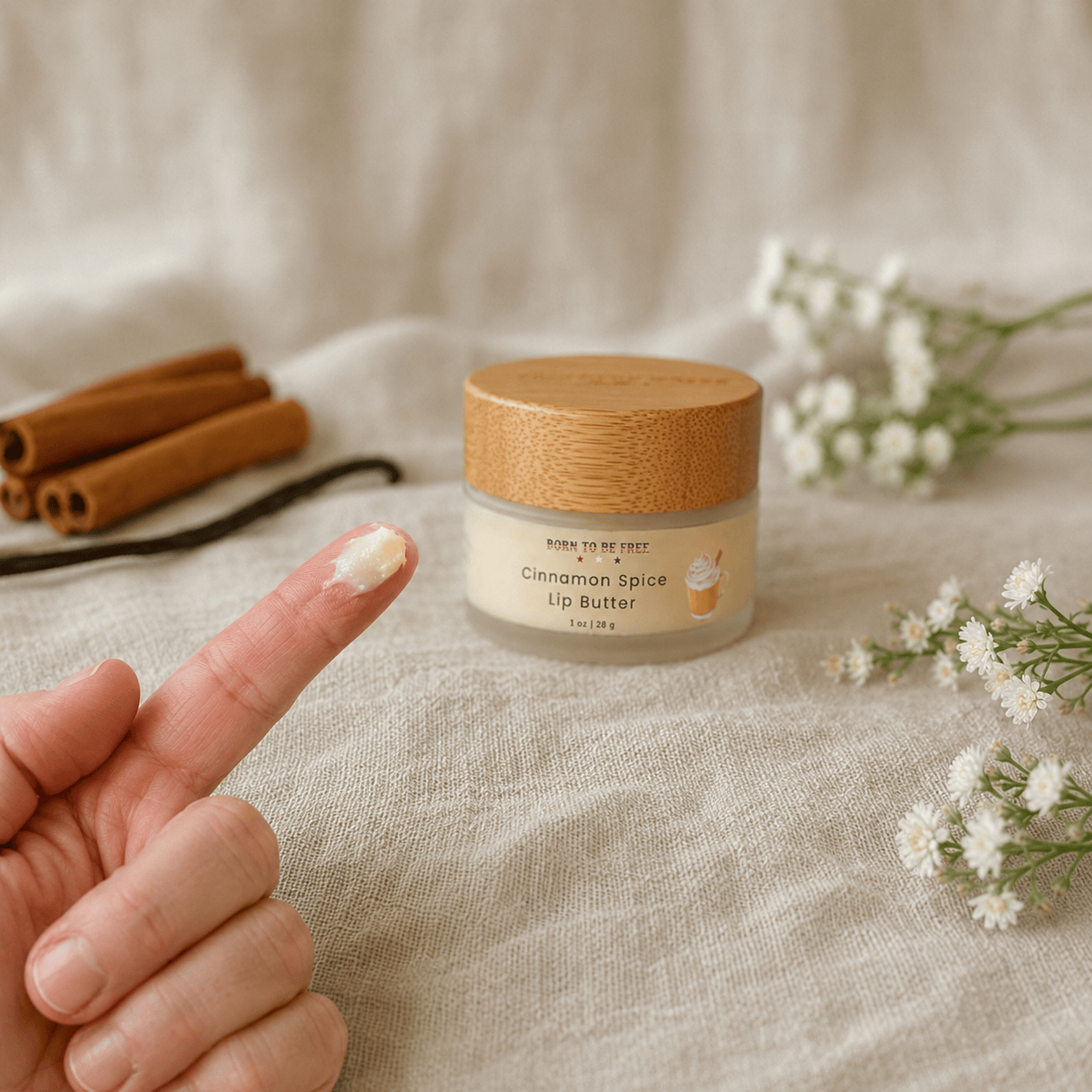 Cinnamon Spice Tallow Lip Butter jar with a finger applying the rich lip treatment, surrounded by cinnamon sticks and flowers.