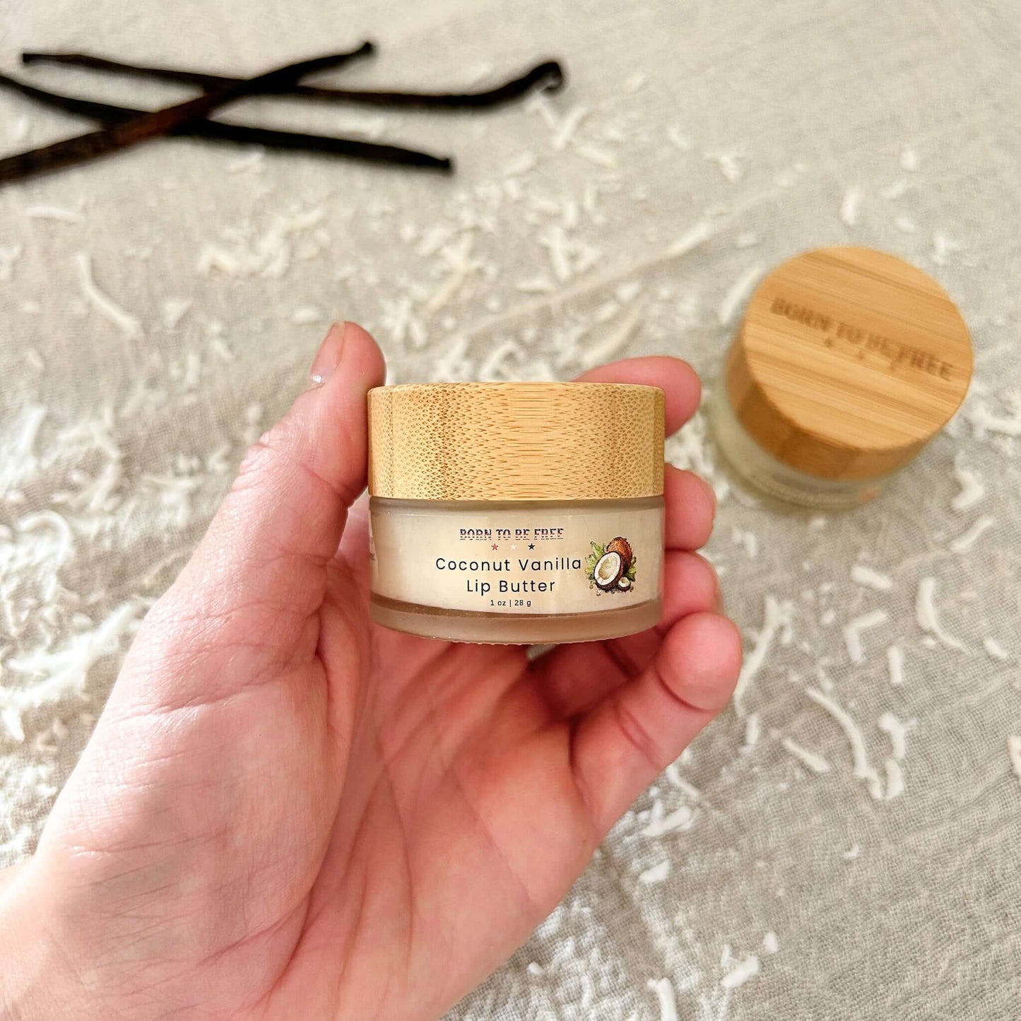 Coconut Vanilla Lip Butter in a jar held by hand, featuring a bamboo lid and tropical coconut design.