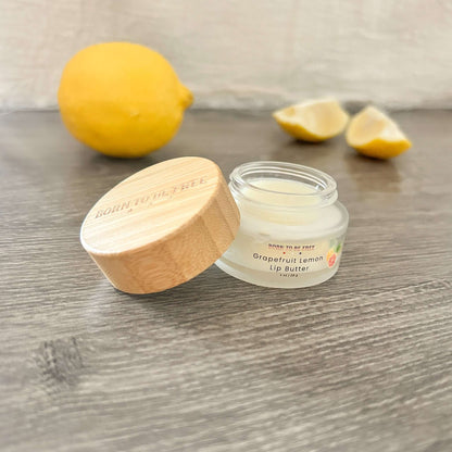 Grapefruit Lemon Lip Butter in a jar with a bamboo lid, surrounded by lemons and lemon slices.