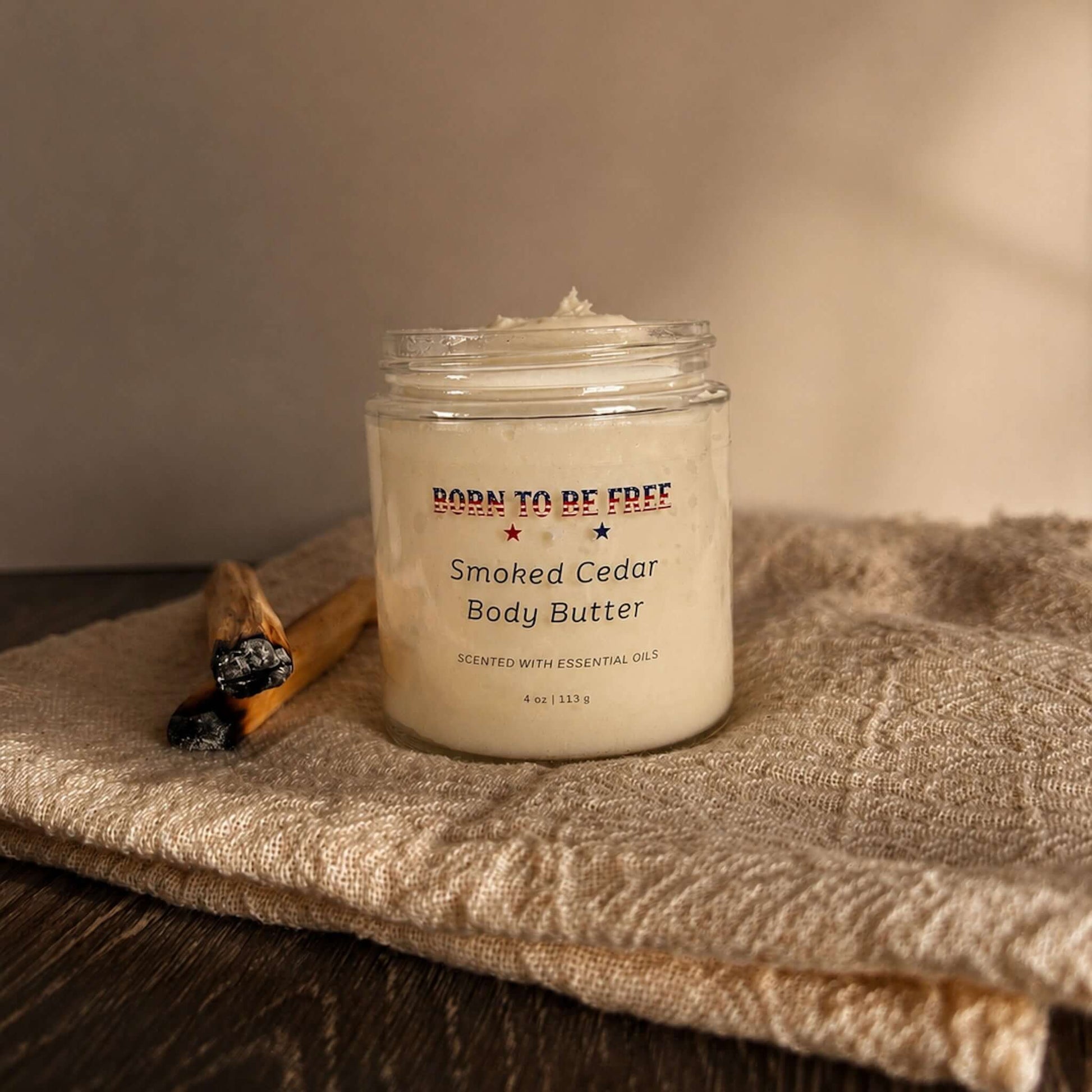 Smoked Cedar Body Butter jar featuring a rich, whipped moisturizer with a woodsy scent on a textured background.