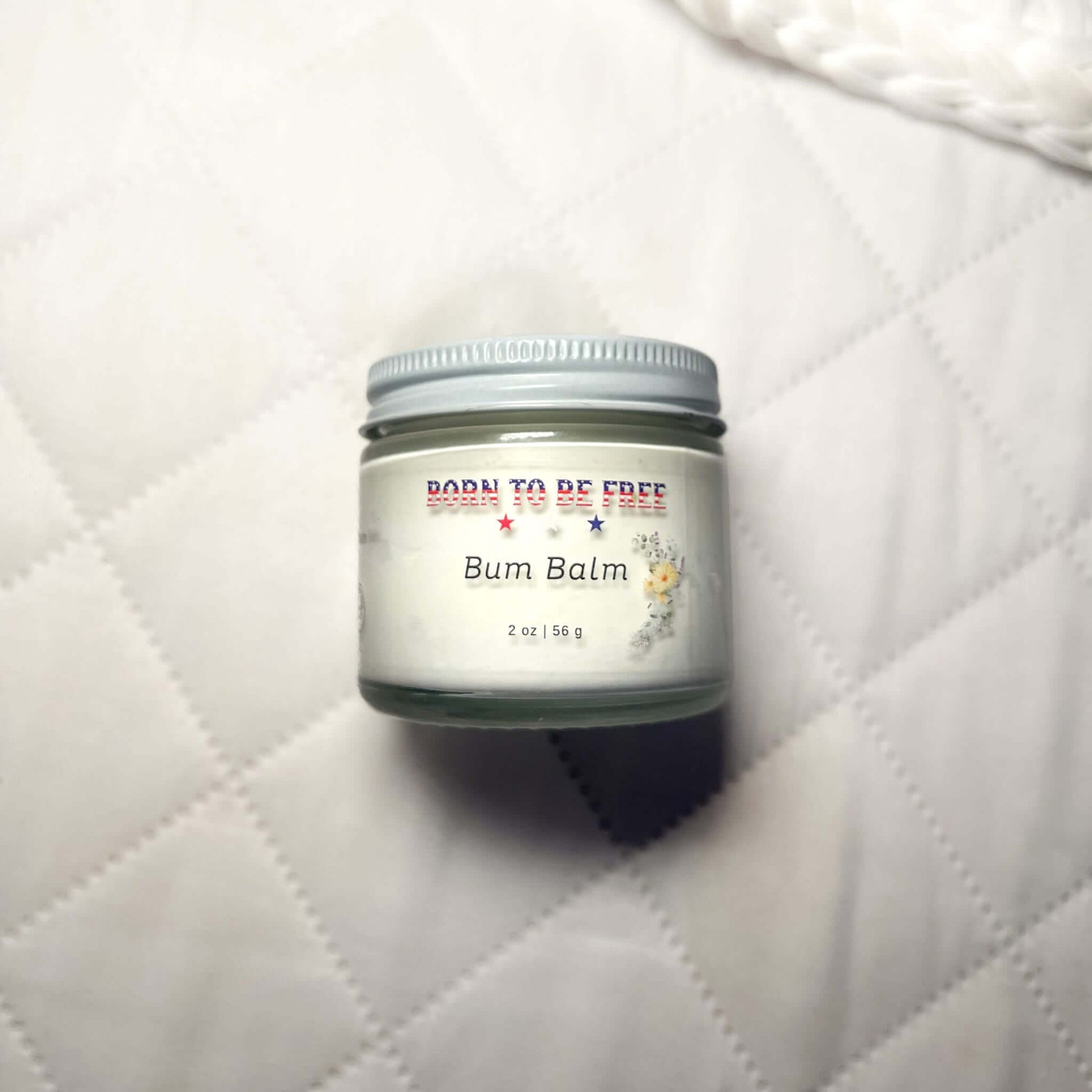 Bum Balm - Baby Diaper Cream with Tallow + Zinc in a 2 oz jar on a soft quilted background.