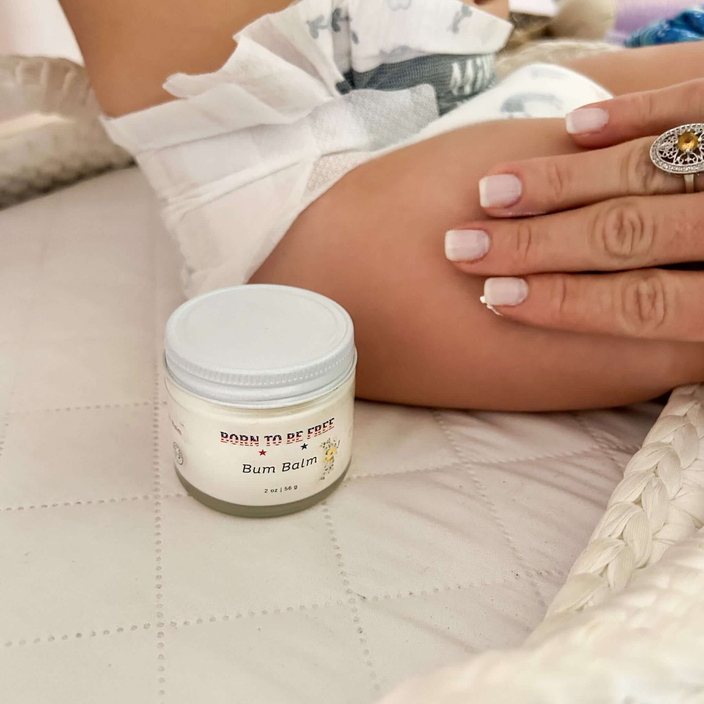 Bum Balm - Baby Diaper Cream with Tallow + Zinc placed next to a baby's leg on a soft surface.
