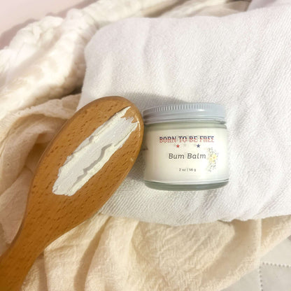 Bum Balm - Baby Diaper Cream with Tallow + Zinc jar on a soft white fabric with a wooden spoon.