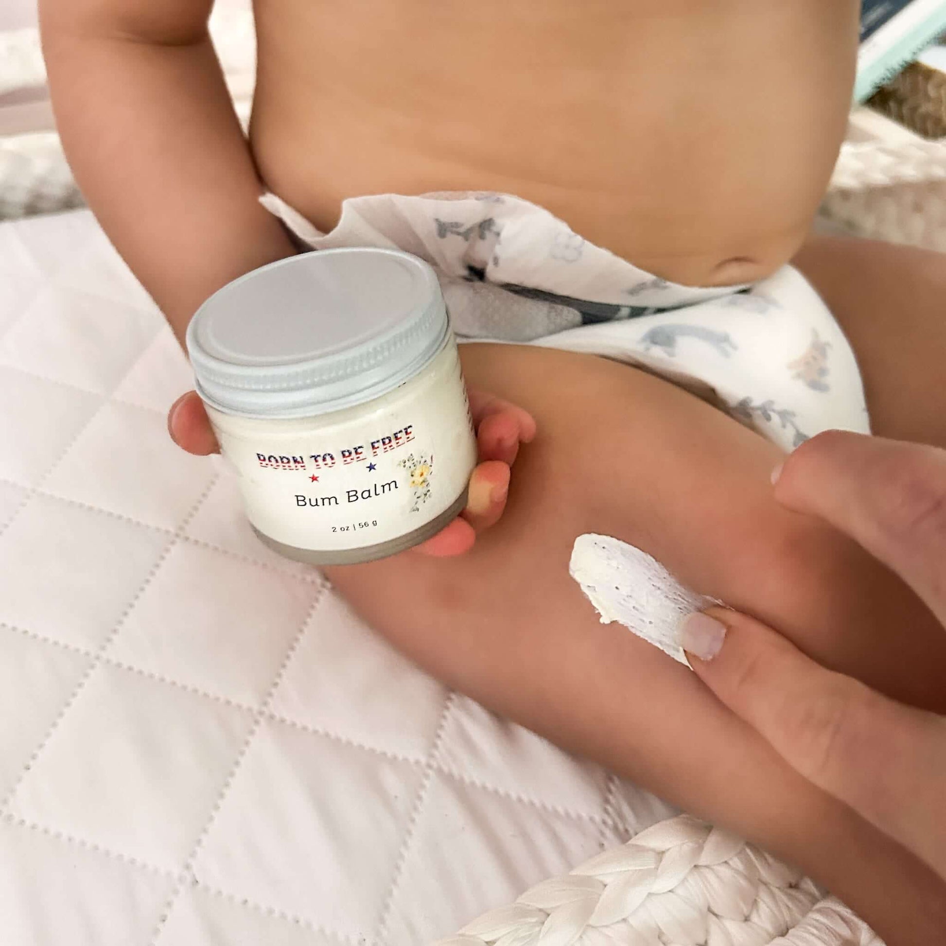 Bum Balm - Baby Diaper Cream with Tallow + Zinc applied on a baby's leg next to the jar.