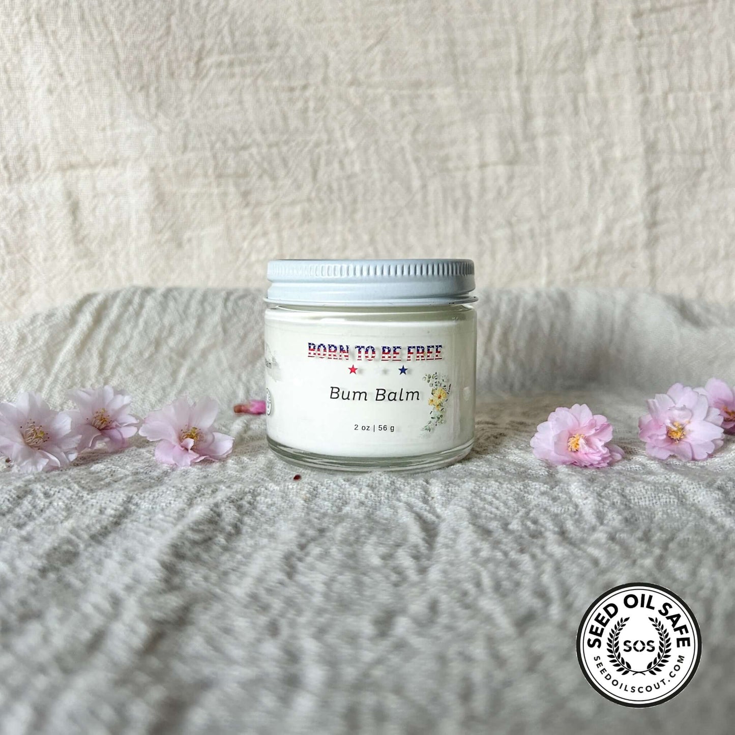 Bum Balm - Baby Diaper Cream with Tallow + Zinc in a glass jar surrounded by pink flowers on a textured background.