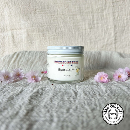 Bum Balm - Baby Diaper Cream with Tallow + Zinc in a glass jar surrounded by pink flowers on a textured background.