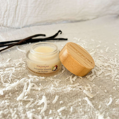 Coconut Vanilla Tallow Lip Butter in a glass jar with bamboo lid, surrounded by coconut shavings and vanilla sticks.