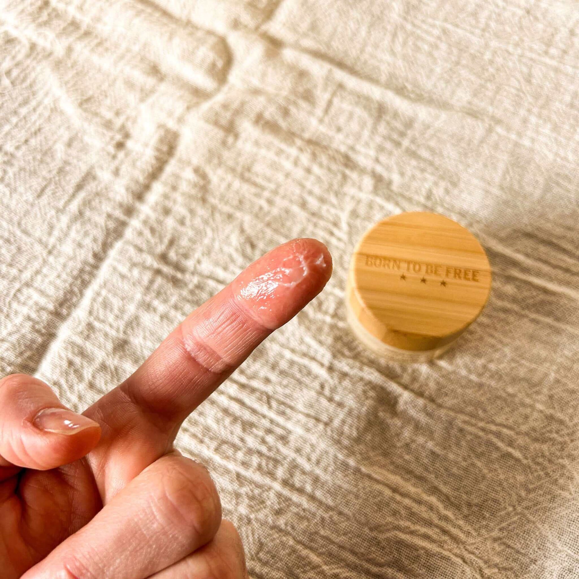 Coconut Vanilla Tallow Lip Butter Grapefruit Lemon Tallow Lip Butter Tallow Lip Butter Set shown on a finger with a wooden container of Vanilla Bean Tallow Lip Butter in the background, highlighting deep nourishment for lips from Sweet Peppermint Tallow Lip Butter and Sweet Almond Tallow Lip Butter