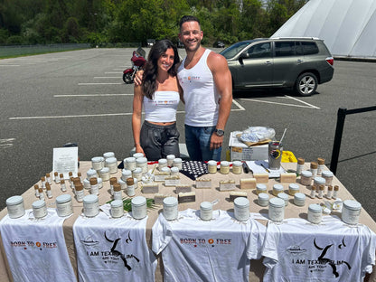 Two vendors at a market showcasing Feeding Forward T-shirts and various products on a table.