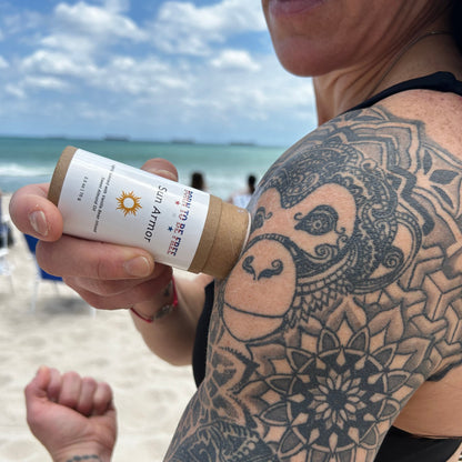 Mineral Based Sun Armor Bundle applied by a person on the beach, showcasing tattoo details and product design.