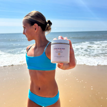 Girl at the beach holding Mineral Based Sun Armor Bundle under sunny skies.