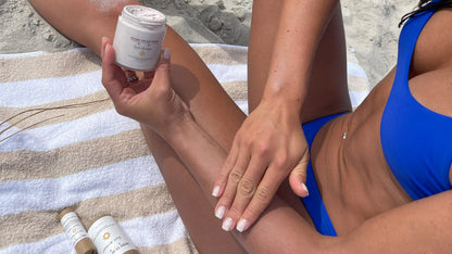 Model applying Mineral Based Sun Armor Bundle on her legs while relaxing on the beach.
