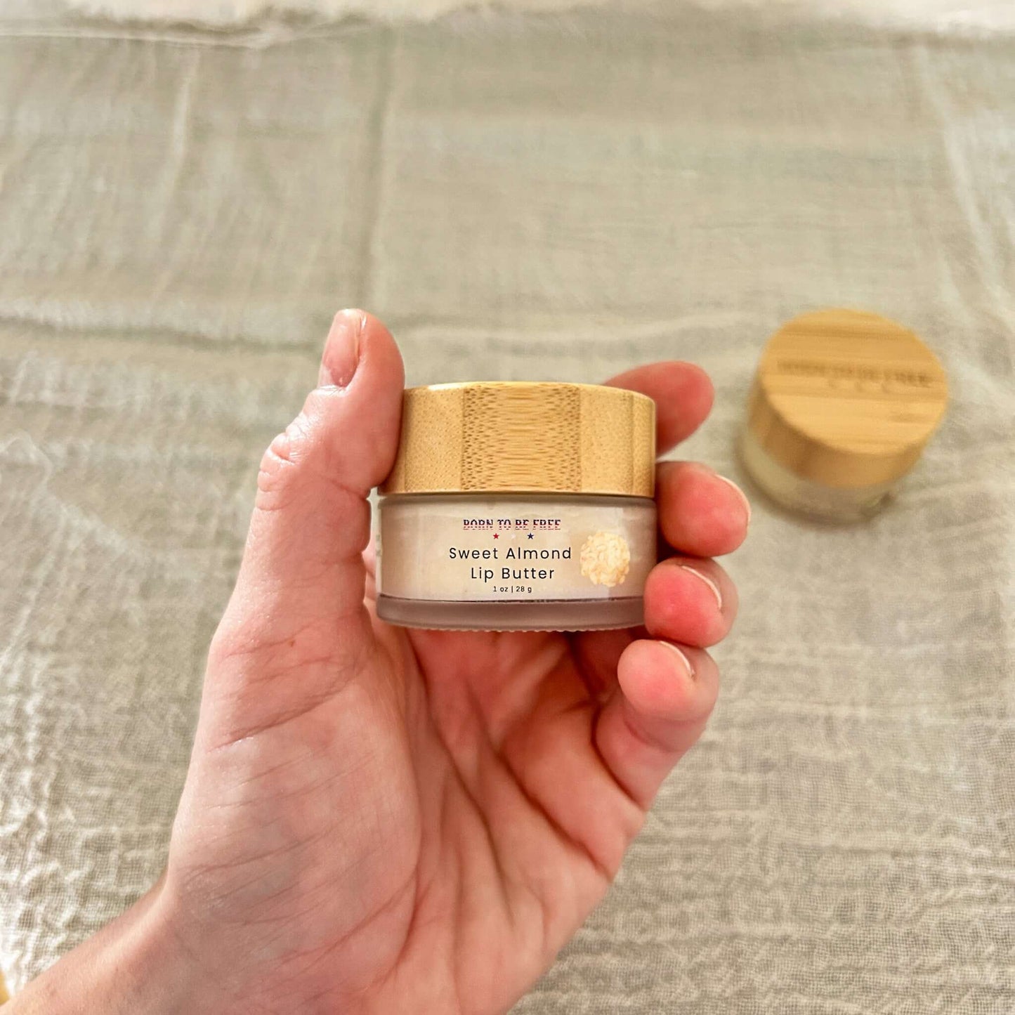 Person holding a jar of Sweet Almond Tallow Lip Butter, showing organic skincare product in a natural setting.