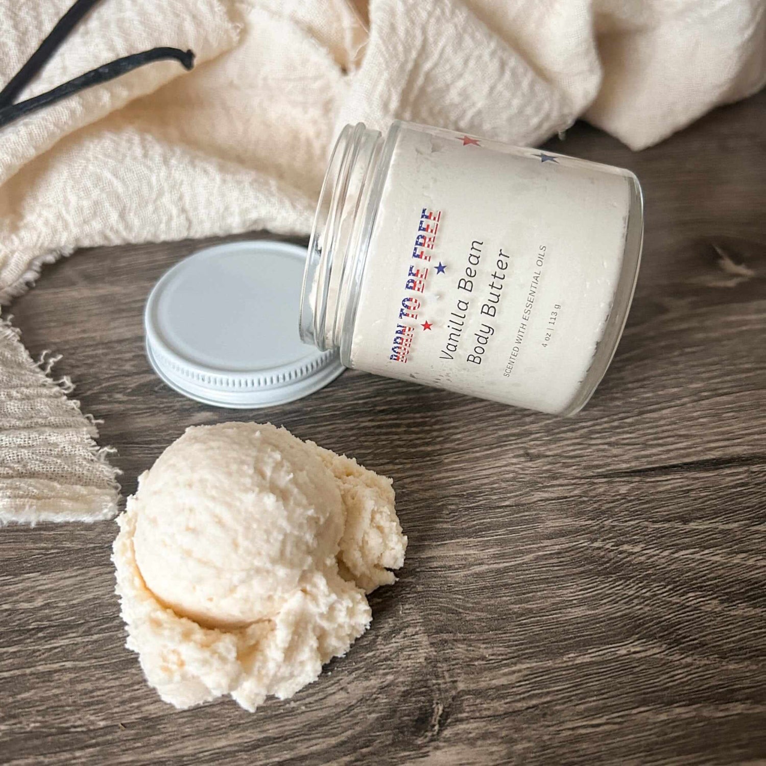 Vanilla Bean Body Butter in a jar with a scoop on a wooden surface, showcasing a rich and creamy texture.