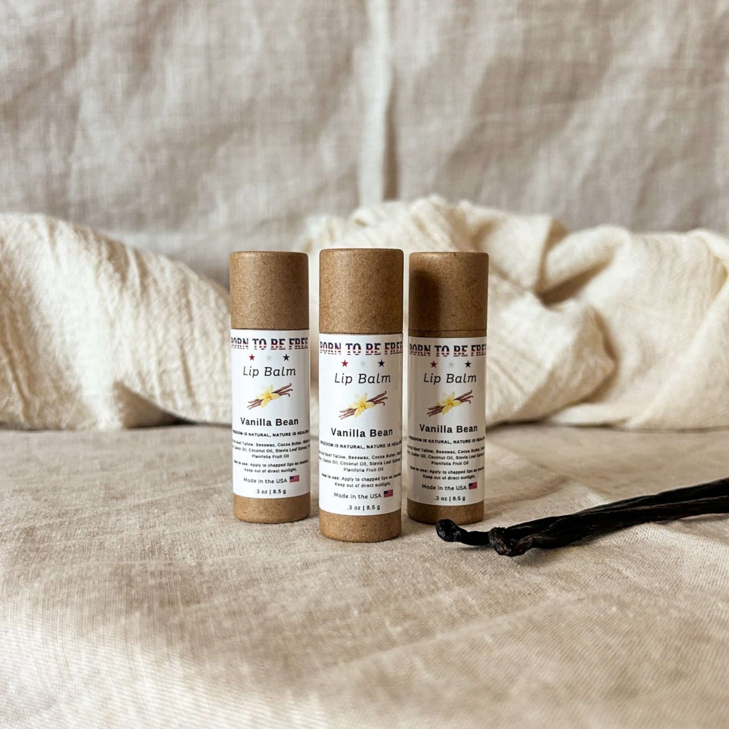 Three tubes of Vanilla Bean Lip Balm on a textured fabric background.