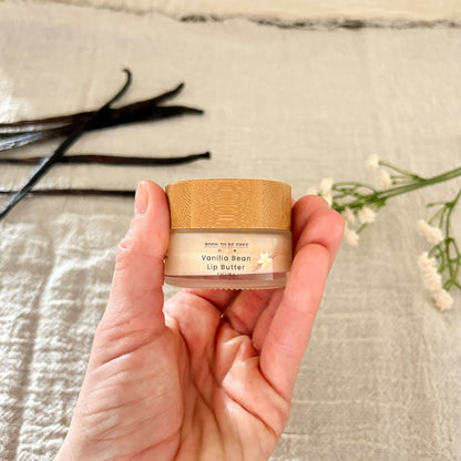 Hand holding a jar of Vanilla Bean Tallow Lip Butter with a bamboo lid, surrounded by natural elements.