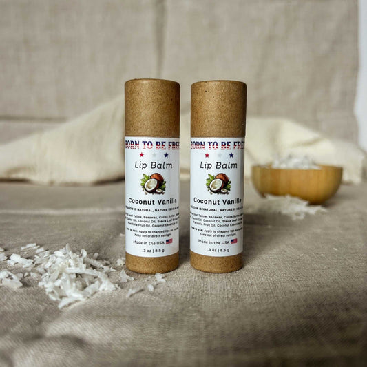 Two Coconut Vanilla Lip Balm tubes on a neutral background with coconut shavings.