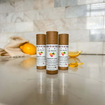 Grapefruit Lemon Lip Balm in eco-friendly packaging on a marble surface with lemon slices and a rustic cloth.