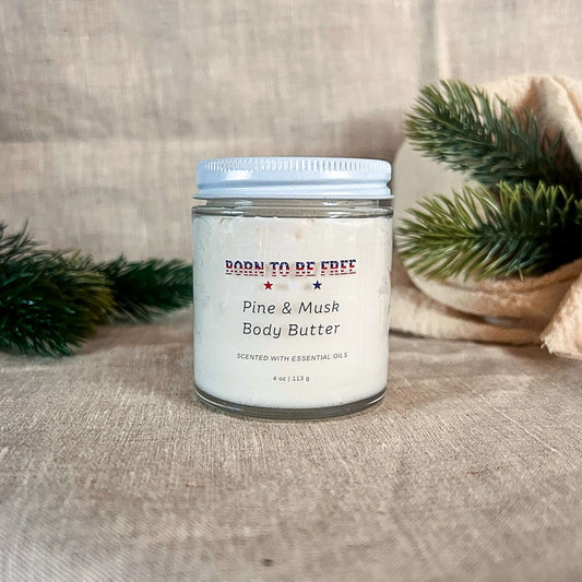 Pine & Musk Body Butter in a jar surrounded by pine branches, showcasing its soothing, natural essence.