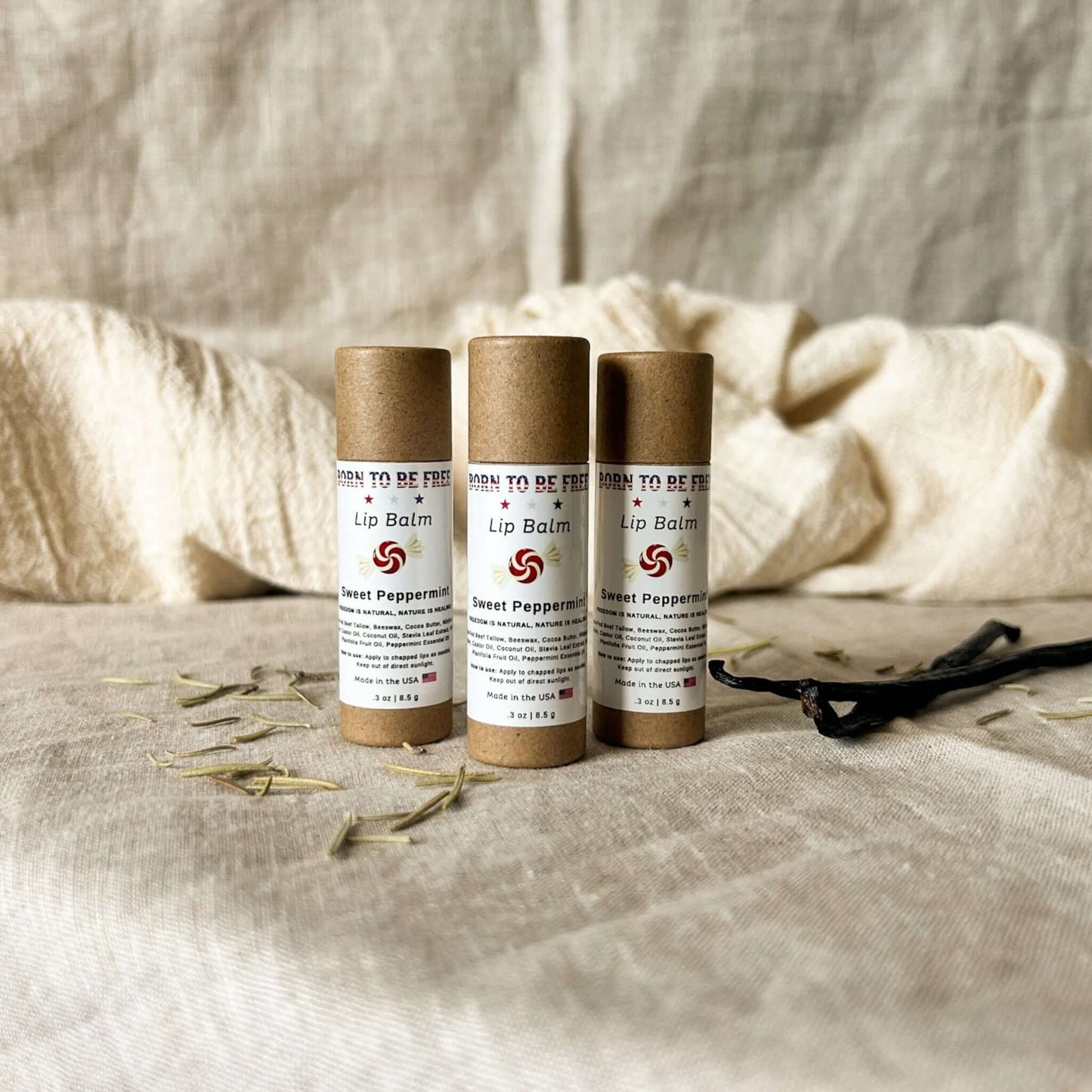 Three tubes of Sweet Peppermint Lip Balm on a soft fabric background, showcasing natural skincare.
