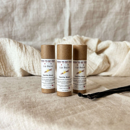 Three tubes of Vanilla Bean Lip Balm on a textured fabric background.