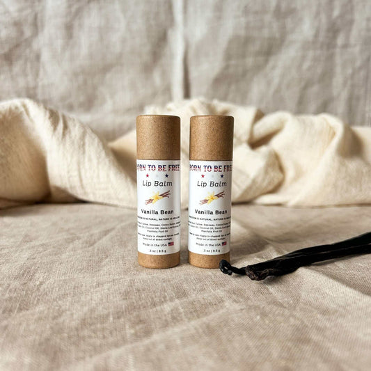 Vanilla Bean Lip Balm tubes displayed on a soft fabric surface with a vanilla pod.